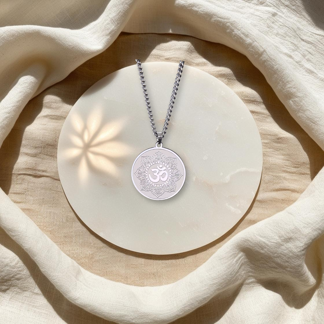 Collier Talisman Lotus & Om en acier inoxydable argenté, posé à plat, dans un environnement lumineux et apaisant d'Âme de Lune, idéal pour la sérénité.