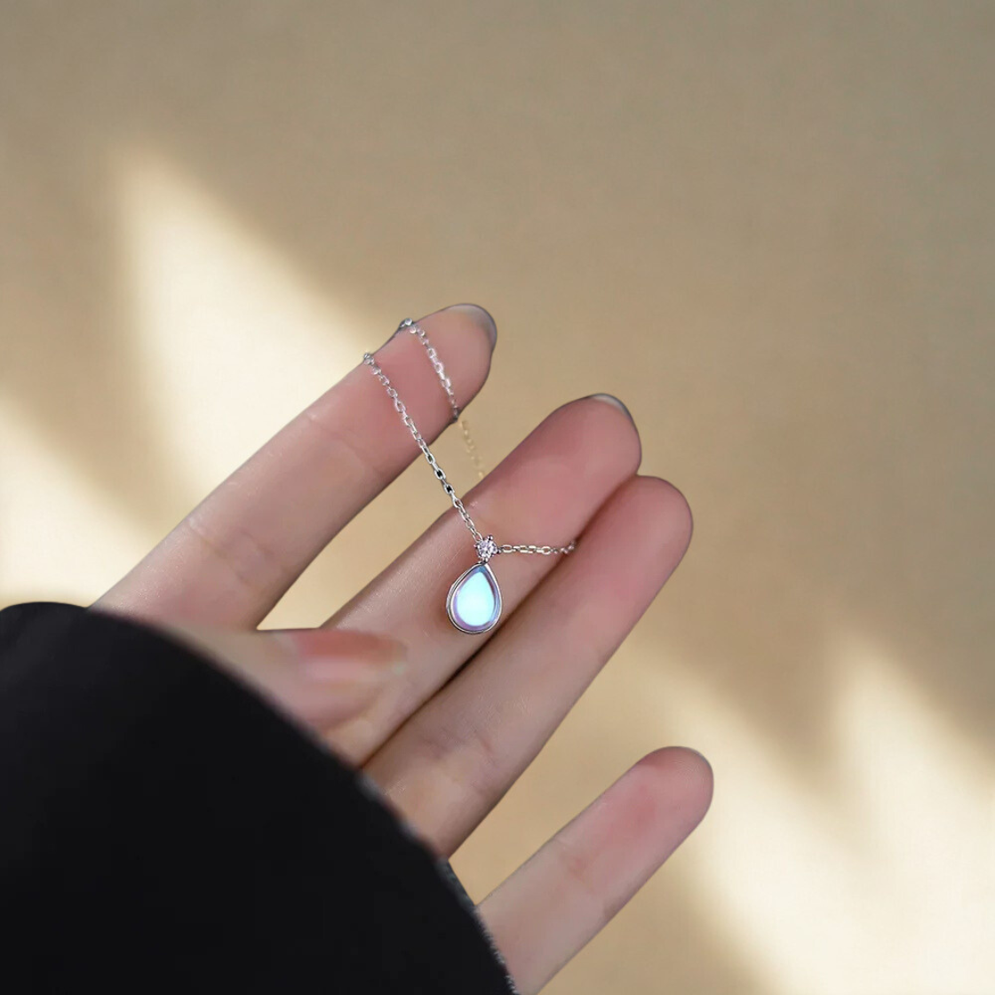 Pendentif en pierre de lune argentée avec reflets bleus, posé délicatement sur une main, lumière douce.