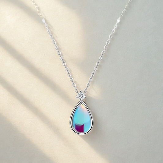 Gros plan d’un pendentif argenté serti d’une pierre de lune à reflets bleus, sur fond beige minimaliste.